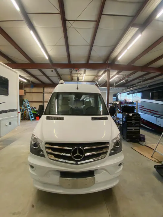White Mercedes Sprinter van (potential RV rental) in a spacious garage with other RVs & workshop equipment.. Airstream Interstate 2017