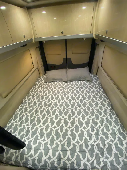 Cozy RV rental sleeping area featuring a bed with grey patterned bedding, pillows, and overhead storage cabinets.. Airstream Interstate 2017