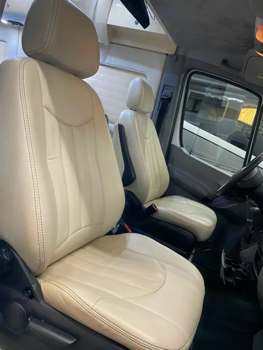 RV rental camper van interior. Shows cream leather driver and passenger seats with armrests and overhead storage compartments.. Airstream Interstate 2017