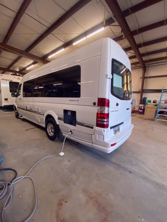 A white Airstream Interstate RV rental is plugged in for maintenance inside a garage next to another RV.. Airstream Interstate 2017