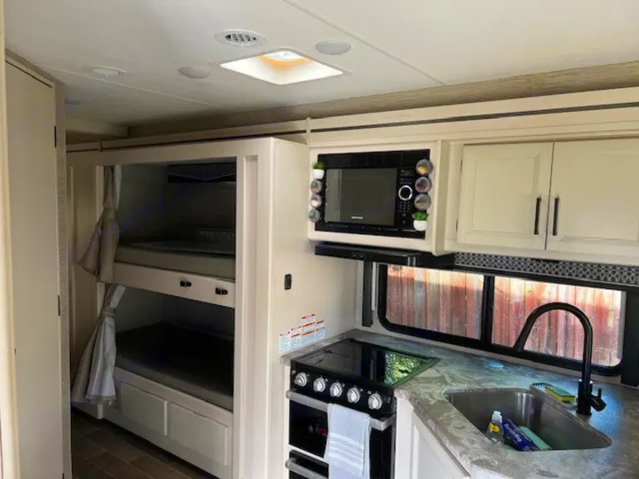 Compact RV rental interior featuring a modern kitchen with microwave, stove, sink, and cozy bunk beds.. Thor Chateau Victory 2022