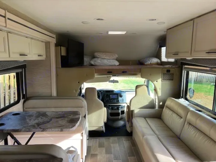 Spacious rv rental interior featuring a dinette, sofa, and cab-over bunk, offering a bright, inviting living space.. Thor Chateau Victory 2022