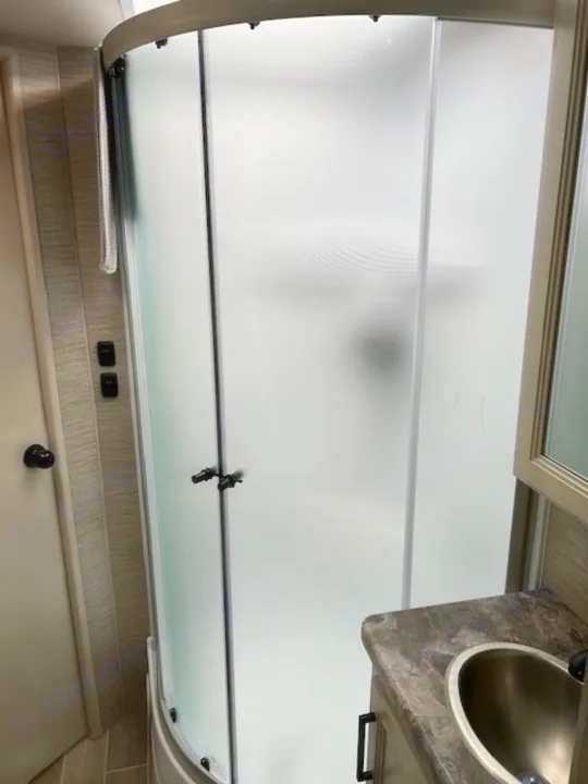 Inside an RV rental: a compact bathroom with a curved frosted glass shower and small vanity with sink.. Thor Chateau Victory 2022