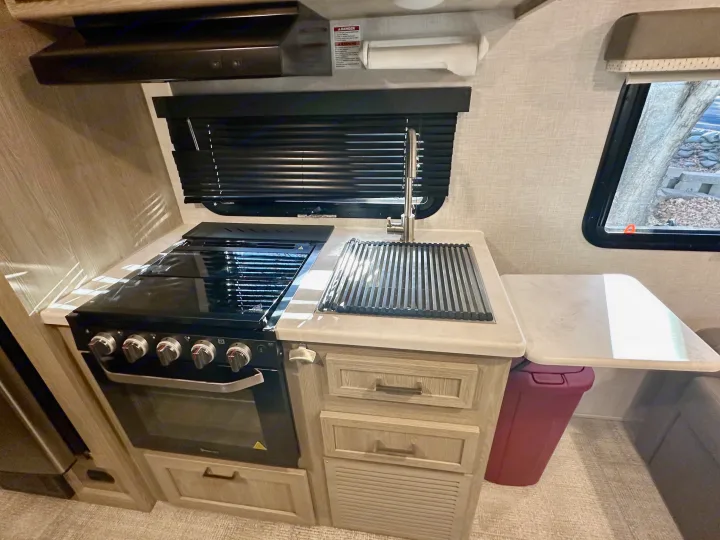 Compact RV rental kitchen with stove, oven, sink, and counter space, complete with a window and range hood.. Forest River Geo Pro 2021