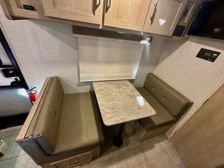 Spacious RV rental dinette with upholstered benches, a table, and overhead storage. Includes safety features like a fire extinguisher.. Forest River Geo Pro 2021