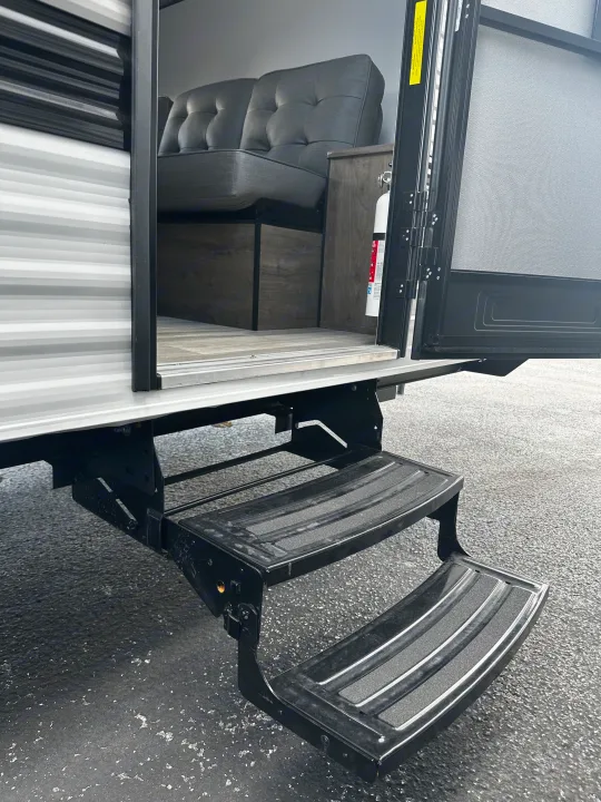 Experience RV rental comfort: Sturdy steps lead to a plush sofa inside this travel trailer, complete with a fire extinguisher.. Heartland RVs Pioneer 2024