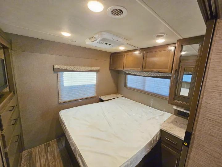 This cozy RV rental bedroom features a bed, overhead cabinets, window with blinds, and AC unit for comfort.. Thor Motor Coach Freedom Elite 2021
