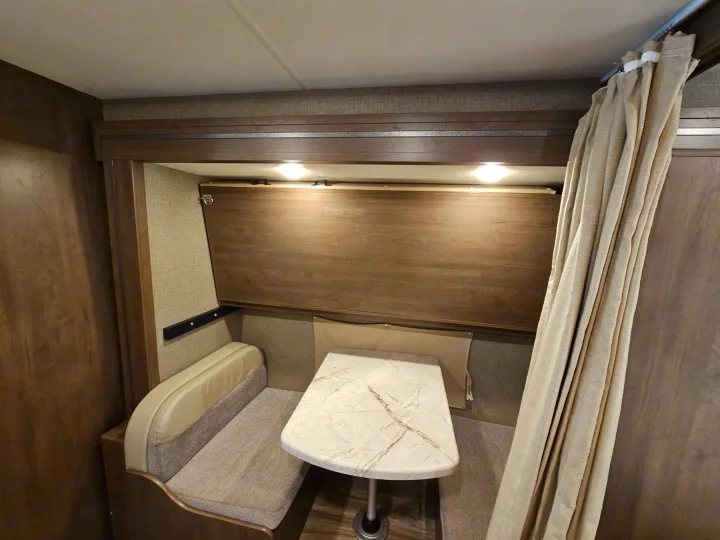 Cozy RV rental dinette with two cushioned bench seats, a marble-patterned table, and overhead wooden panel.. Thor Motor Coach Freedom Elite 2021
