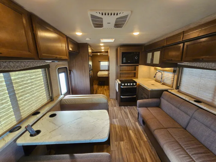 Modern RV rental interior showing a full kitchen, dining area, sofa, and a glimpse of the back bedroom.. Thor Motor Coach Freedom Elite 2021