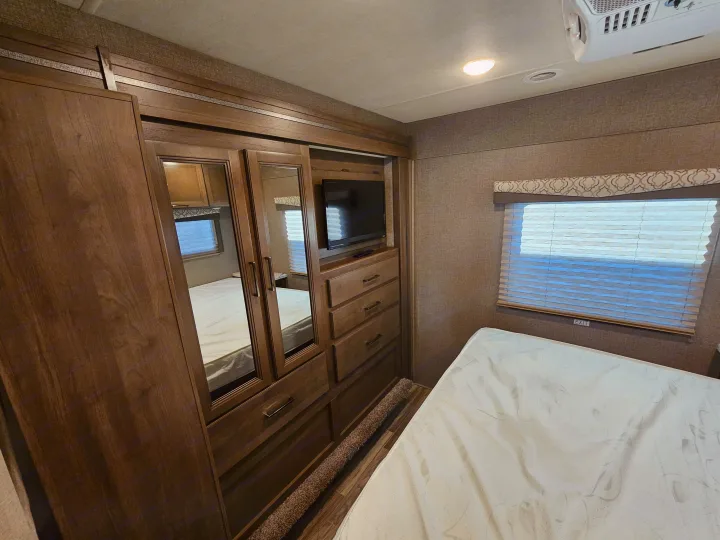 Spacious RV rental bedroom with a comfortable bed, mirrored wardrobe, TV, and ample storage for a cozy stay.. Thor Motor Coach Freedom Elite 2021