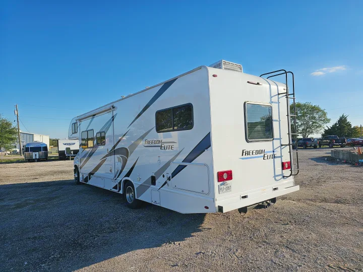 White Freedom Elite motorhome, available for RV rental, parked on a gravel lot under a clear blue sky. Texas license plate visible.. Thor Motor Coach Freedom Elite 2021