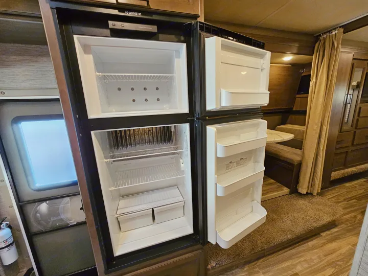 Inside an RV rental: empty Dometic refrigerator with freezer, shelves, and door bins ready for travel.. Thor Motor Coach Freedom Elite 2021