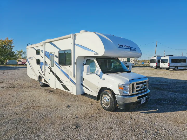 A bright white Thor Freedom Elite RV rental with blue accents, parked on a gravel lot under a clear blue sky.. Thor Motor Coach Freedom Elite 2021