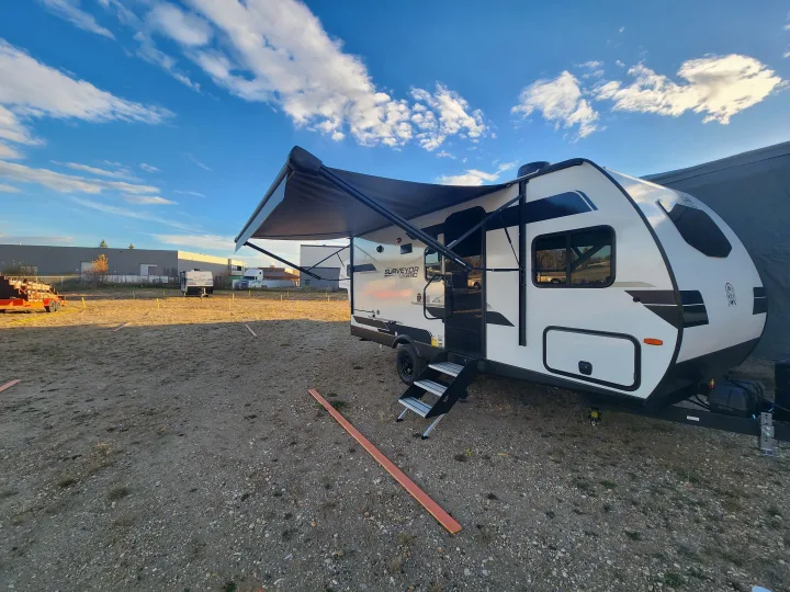 Experience outdoor adventure with this Surveyor Legend RV rental, parked on a gravel lot under a blue sky.. Forest River Surveyor 19BHLE 2024