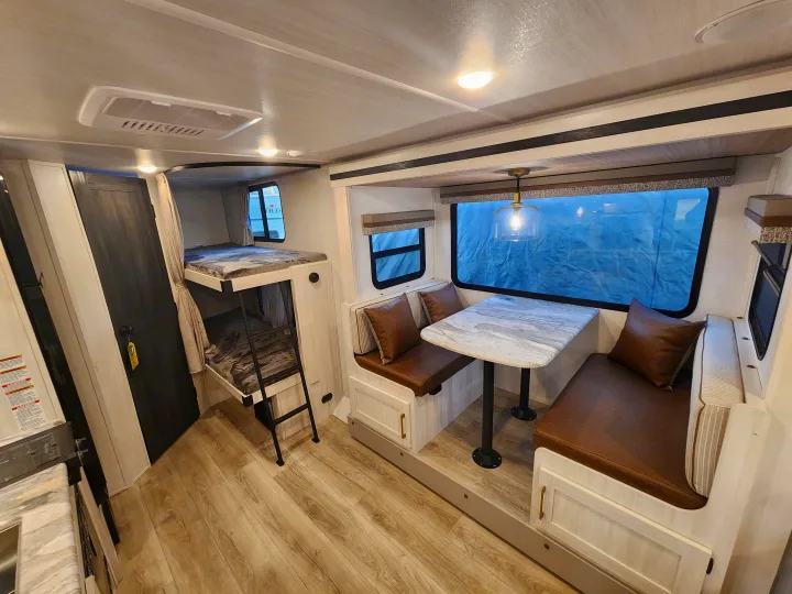 Experience comfort in this RV rental! Features bunk beds, a dinette with brown cushions, and modern light wood interior.. Forest River Surveyor 19BHLE 2024