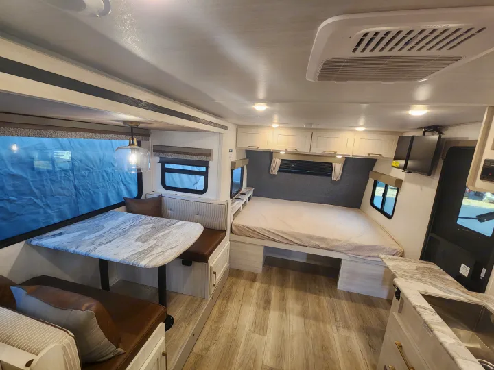 Inside a modern rv rental showing a dinette, comfy bed, and small kitchen setup. Perfect for your next adventure.. Forest River Surveyor 19BHLE 2024