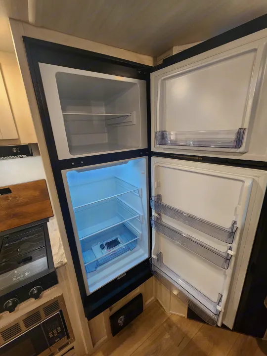 Bright, open RV rental refrigerator & freezer with shelves & door bins, ready for your adventure.. Forest River Surveyor 19BHLE 2024