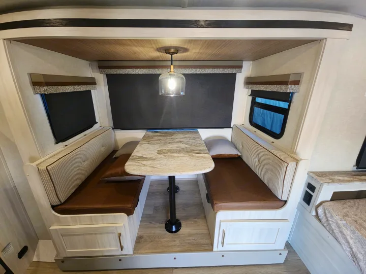RV rental dinette: light wood interior with brown booth seating, marble-look table, and windows.. Forest River Surveyor 19BHLE 2024