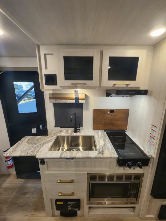 RV rental kitchen with granite-look countertops, stainless steel sink, stove, microwave, and light wood cabinetry.. Forest River Surveyor 19BHLE 2024