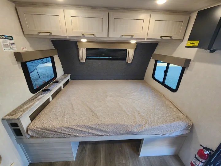 Spacious RV rental bedroom with a large bed, overhead cabinets, and dual windows for a comfortable night's sleep on your adventure.. Forest River Surveyor 19BHLE 2024