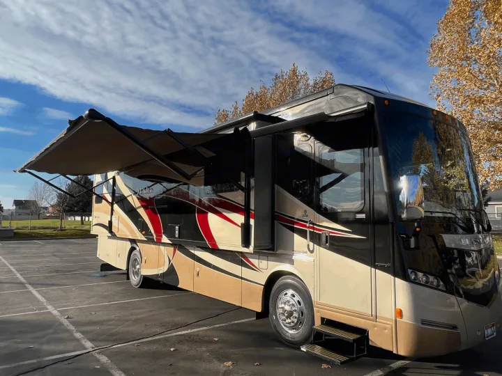 Luxurious tan & black RV rental with red accents, awning extended, parked for your next travel adventure.. Itasca Meridian 2014
