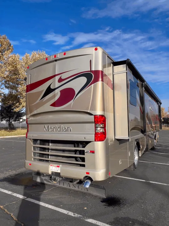A sleek, golden Meridian motorhome, with its slide-out extended, parked on asphalt. Explore the open road with an RV rental!. Itasca Meridian 2014
