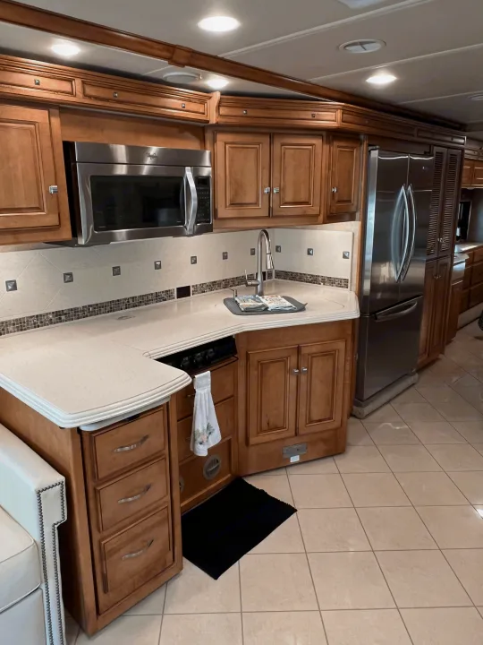 Inside an RV rental, this full kitchen features wood cabinets, stainless appliances, bright counters, and tile floors for comfortable trips.. Itasca Meridian 2014