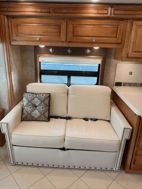 Comfortable light-colored RV sofa with seatbelts, wooden cabinets, and a window view, perfect for your next rv rental.. Itasca Meridian 2014