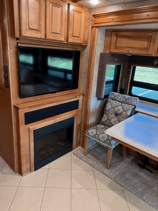 RV rental's inviting living space: TV, fireplace, wooden cabinets, dining area with a patterned chair, and a white table.. Itasca Meridian 2014