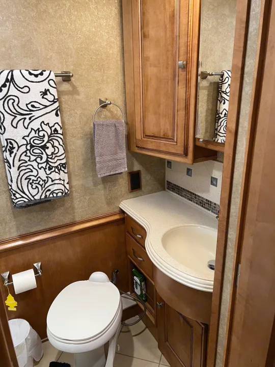 This RV rental's well-equipped compact bathroom features a toilet, sink vanity, and essential amenities for comfortable travel.. Itasca Meridian 2014