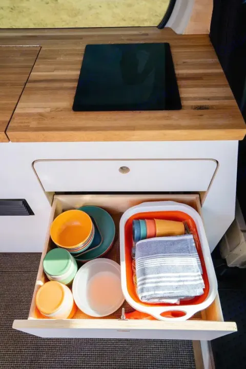 RV rental kitchen setup: Open drawer reveals compact, colorful dishes, cups, and accessories for organized campervan living.. VanCraft VanCraft Class B 2022