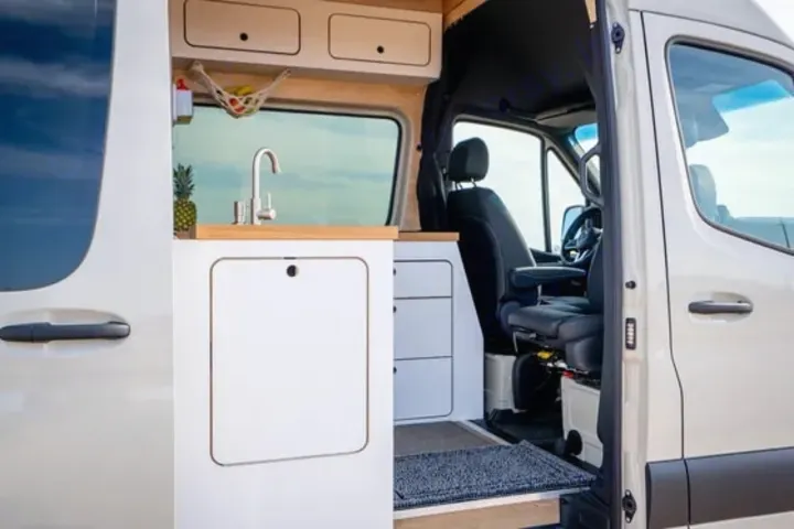 Modern RV rental interior: compact kitchen with sink, storage, and the van's driver cabin visible.. VanCraft VanCraft Class B 2022