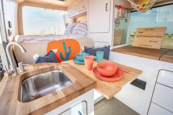 This RV rental features a cozy camper van interior with a modern kitchen sink, dining area, and rear bed.. VanCraft VanCraft Class B 2022
