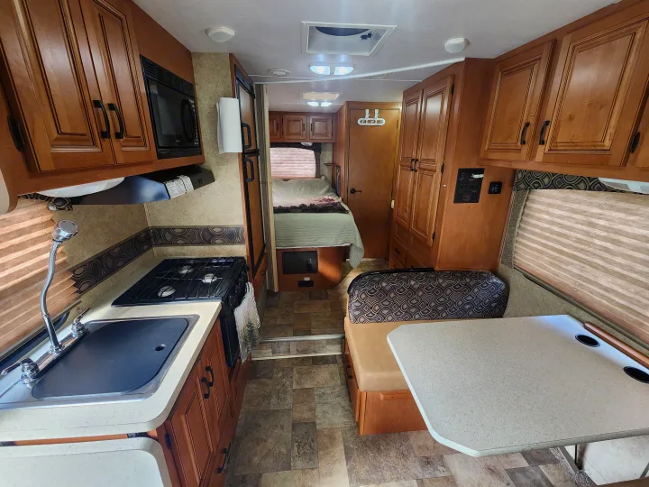 Functional RV rental interior featuring a kitchen, dinette, bed, and wood cabinets.. Forest River Sunseeker 2014