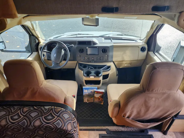 Get ready to explore in this RV rental! Interior view of the cockpit with front seats, dashboard, and travel guide magazines.. Forest River Sunseeker 2014