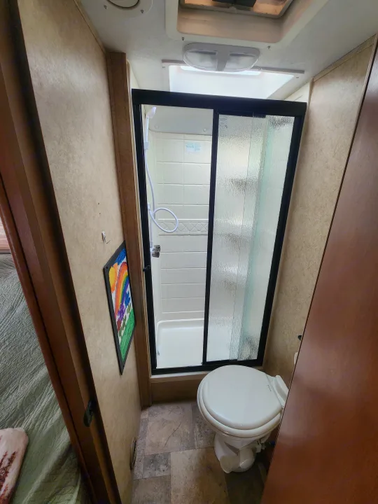 RV rental bathroom featuring a compact shower with a glass sliding door and a toilet, ideal for travel.. Forest River Sunseeker 2014