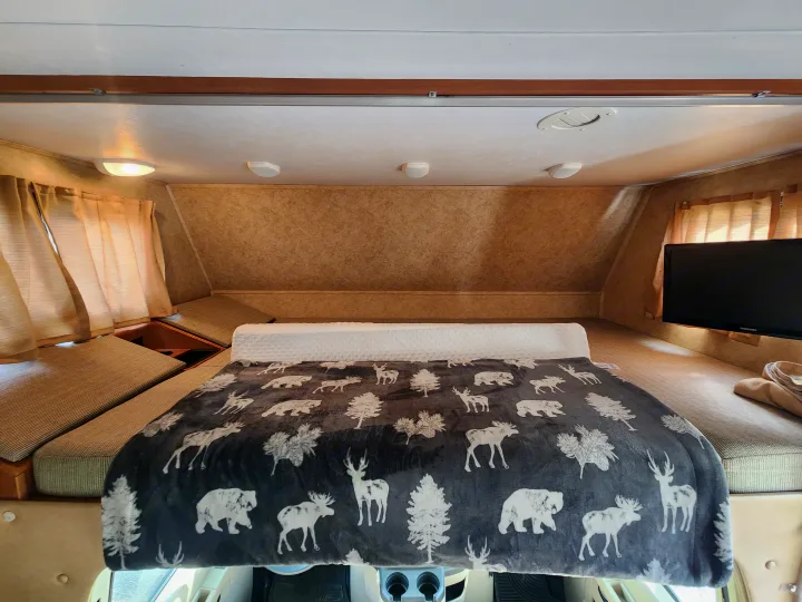 Cozy RV rental cab-over bunk bed features a wilderness blanket, storage, and TV, perfect for a comfortable journey.. Forest River Sunseeker 2014