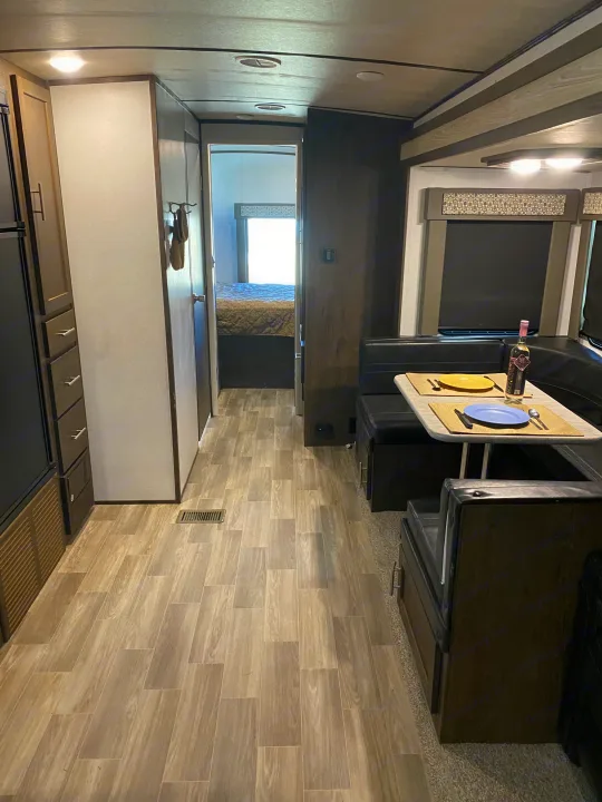 Inside an RV rental: a dining booth with table set, kitchen/pantry on left, leading to a rear bedroom.. Forest River Salem Hemisphere GLX 2019