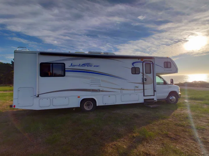 RV rental enjoying a coastal sunset view. A white motorhome is parked by the ocean under a cloudy sky.. Jamboree Jamboree Motorhome 2011