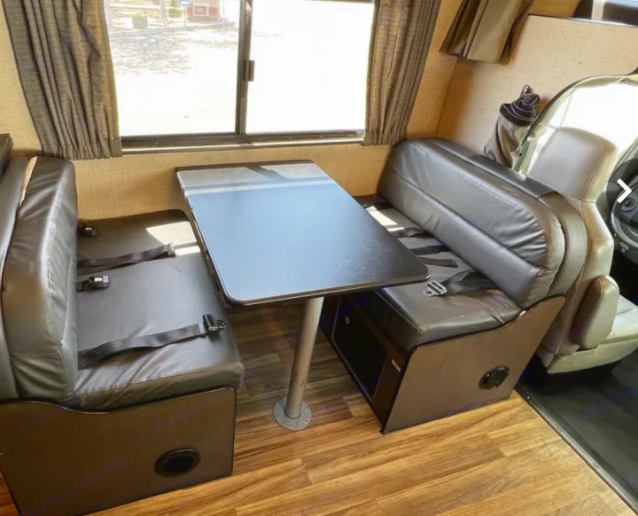 An RV rental's dinette features black upholstered benches with seatbelts and a central table, ready for travel.. Thor Majestic 2019