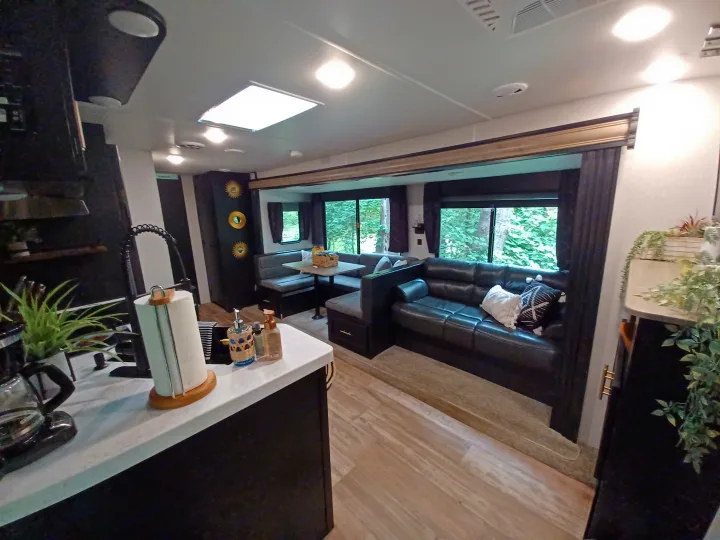 Modern RV rental interior: living space with dining booth, comfy couch, and kitchen counter for enjoyable travels.. Forest River Cherokee 2021