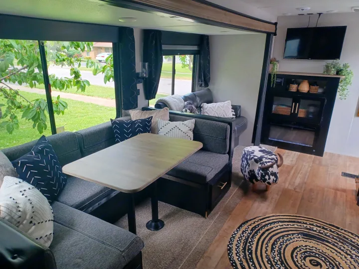 Modern RV rental interior with a cozy dining booth, living area with TV & fireplace, and outdoor view.. Forest River Cherokee 2021