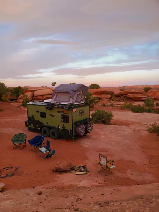 Off-road Xplore RV rental trailer amidst red rock desert at dusk. Campsite ready with chairs for adventure seekers.. Imperial Outdoors XploreRV 2023
