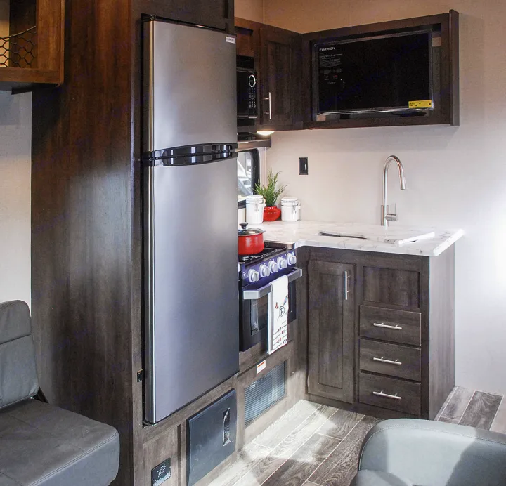Explore this modern RV rental kitchen, featuring a full-size fridge, stove, sink, microwave, and ample storage.. K-Z Manufacturing Sportster 2019