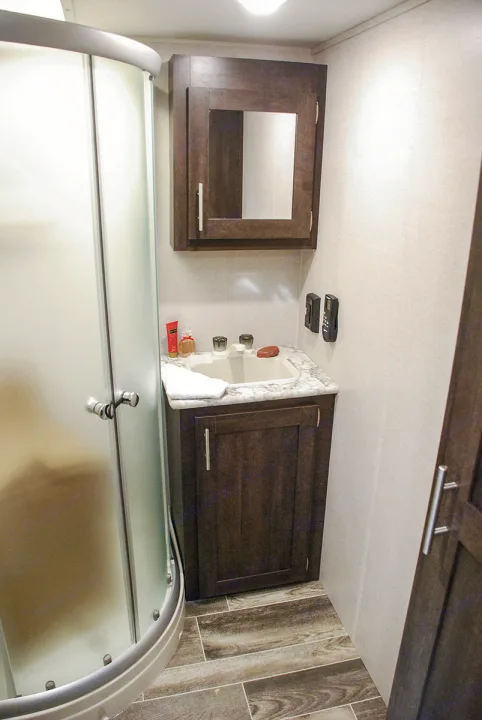Compact RV rental bathroom: curved shower, dark wood vanity with sink, mirrored medicine cabinet. Ideal for travel.. K-Z Manufacturing Sportster 2019
