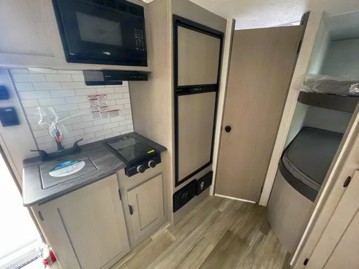 RV rental interior featuring a compact kitchen with microwave, sink, stovetop, refrigerator, and cozy bunk beds.. Coachmen Clipper 2024