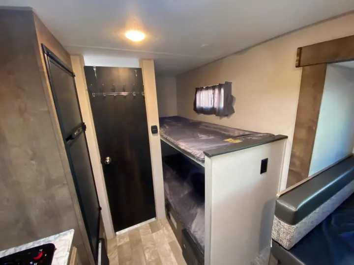 An RV rental's cozy interior: bunk beds, fridge, bathroom door, and dinette visible, ideal for travels.. KZ Sportsman 2020