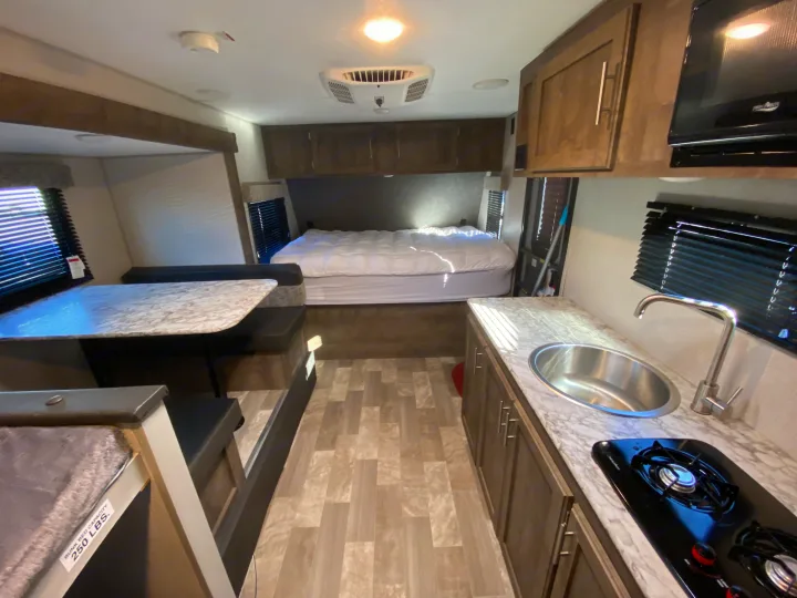 Inside a spacious RV rental: cozy bed, dinette, kitchen with sink & stove, plus a bunk bed (250 lbs capacity).. KZ Sportsman 2020