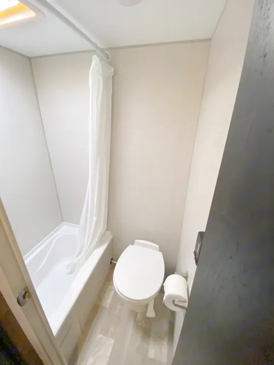 Clean RV rental bathroom showcasing a compact white tub/shower, toilet, and light walls with a skylight.. KZ Sportsman 2020
