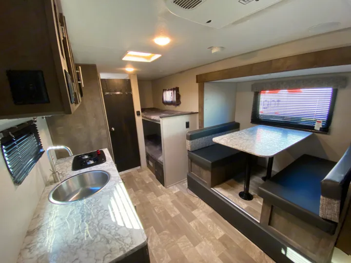 This RV rental interior features a kitchen with sink and stovetop, a cozy dinette, and convenient bunk beds for comfortable travel.. KZ Sportsman 2020